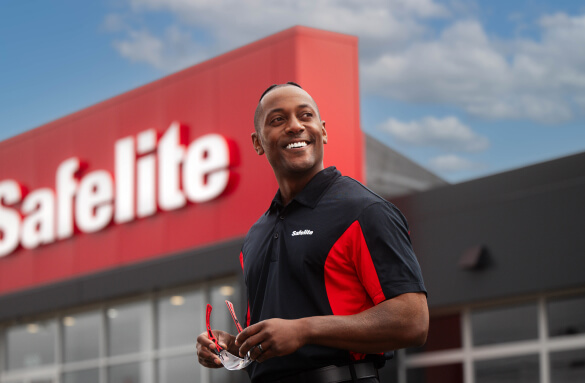 A Safelite technician smiling outside of a Safelite shop.